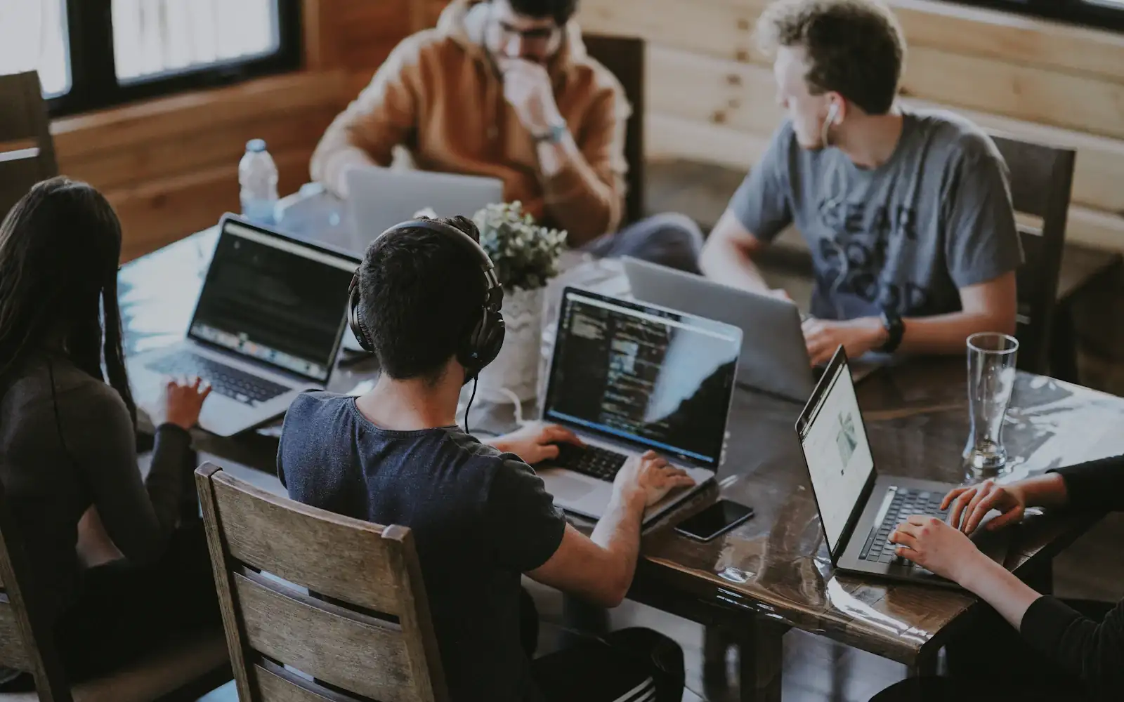 Five people at one wooden table, each reading from their own laptop screen